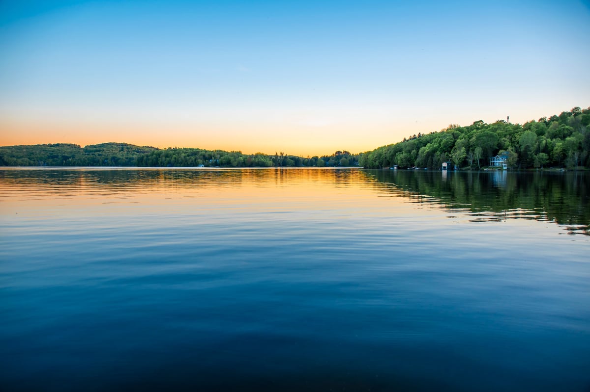 A lake house sits on the shore of the calm water of Peninsula Lake near Huntsville, Ontario on a clear summer evening