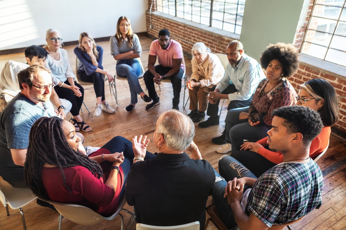Diverse group in a circle, discussing in a bright room. Mixed genders, engaged in conversation