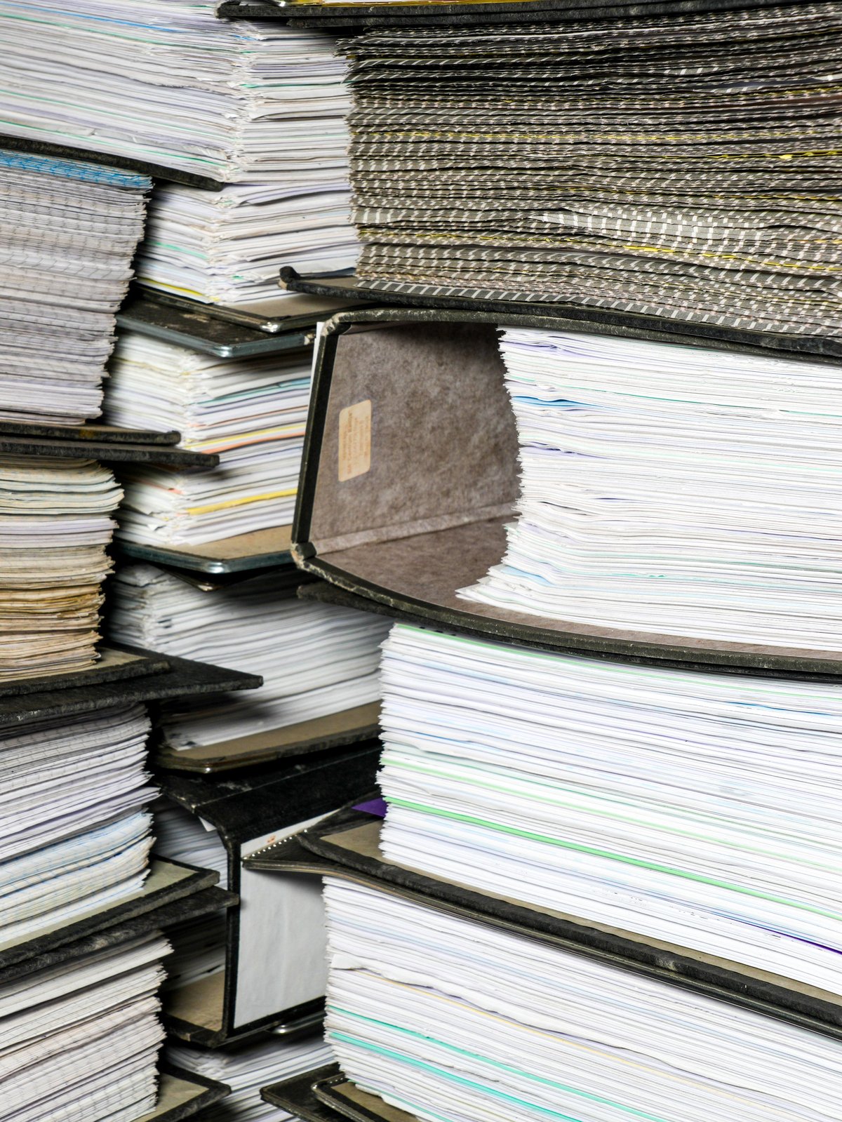 Densely stacked accounting document folders filled with paperwork, showing office archives, bookkeeping, audits, and administrative workload